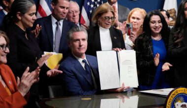 Newsom sitzt an seinem Gouverneurstisch und hält das Dokument in die Kameras. Hinter und neben ihm stehen zahlreiche Parteifreunde.