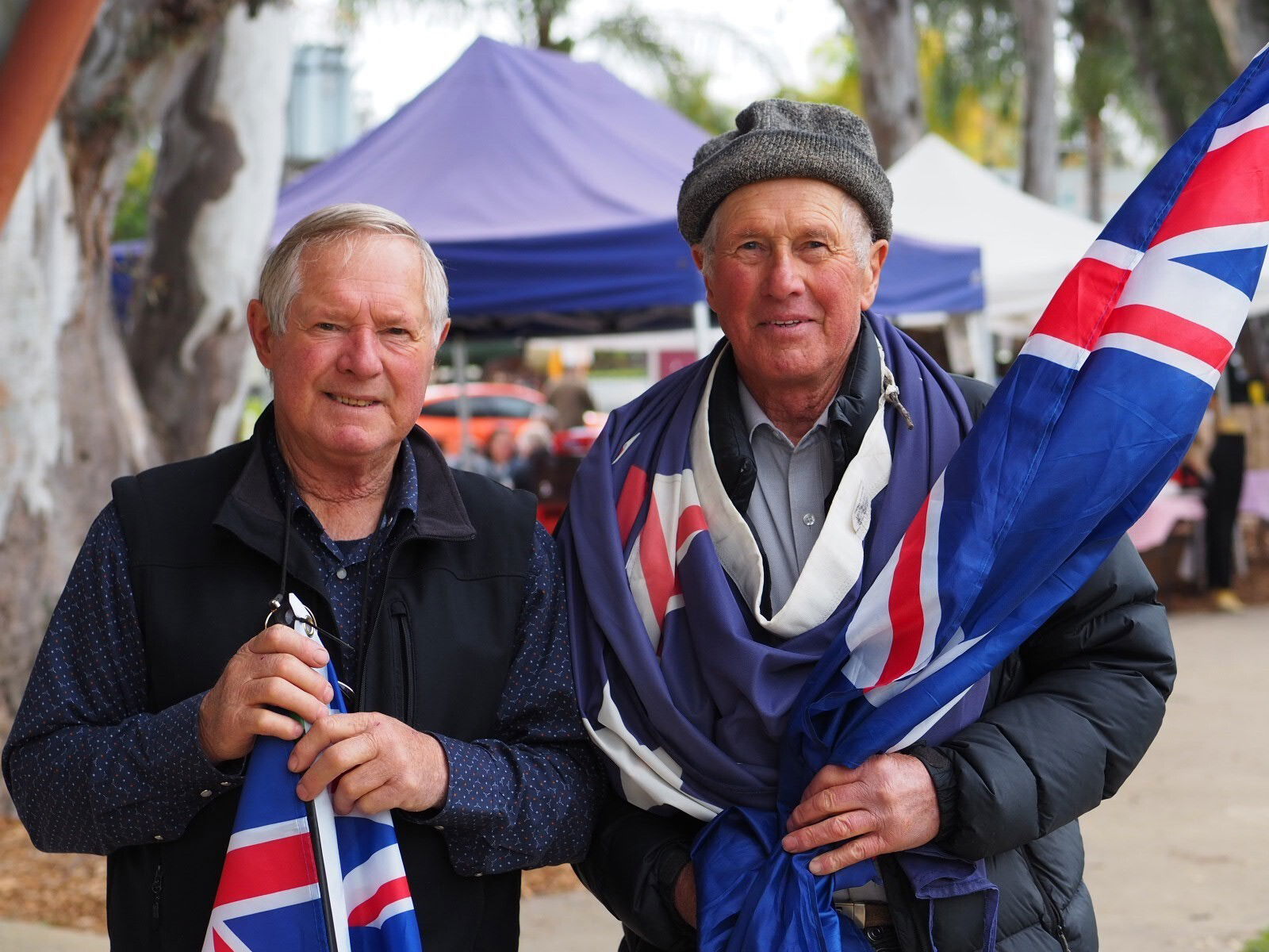 Two older white men smile at the camera holding Australian flags.