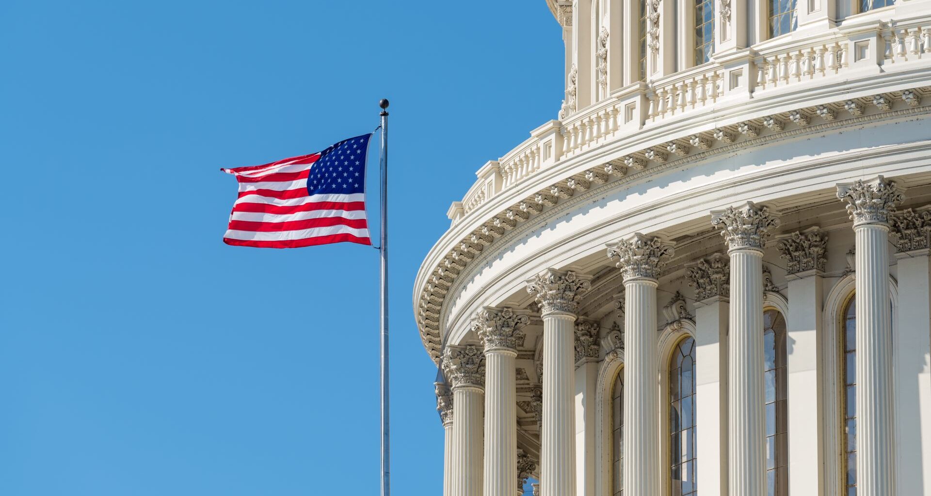 An American flag flying outside the US Capitol building against a blue sky