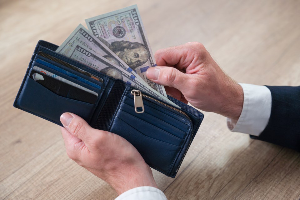 Man's hands holding a wallet with US hundred-dollar bills.