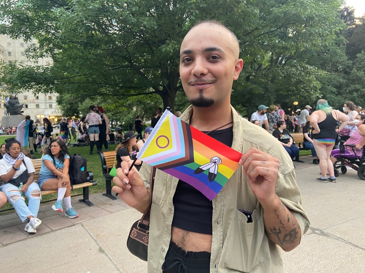 A man holding a pride flag poses for a photo at confederation park. 