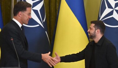 NATO-Genralsekretär Rutte und der ukrainische Präsident Selenskyj reichen sich die Hand. Hinter ihnen die NATO- und die Ukraine-Flagge.
