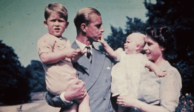 Prince Philip holding Prince Charles while Princess Anne, held by Queen Elizabeth, pulls on his lip