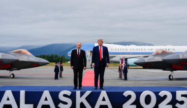 US-Präsident Donald Trump und der russische Präsident Wladimir Putin stehen auf einem Flughafen auf einem Podest, auf dem "Alaska 2025" steht.