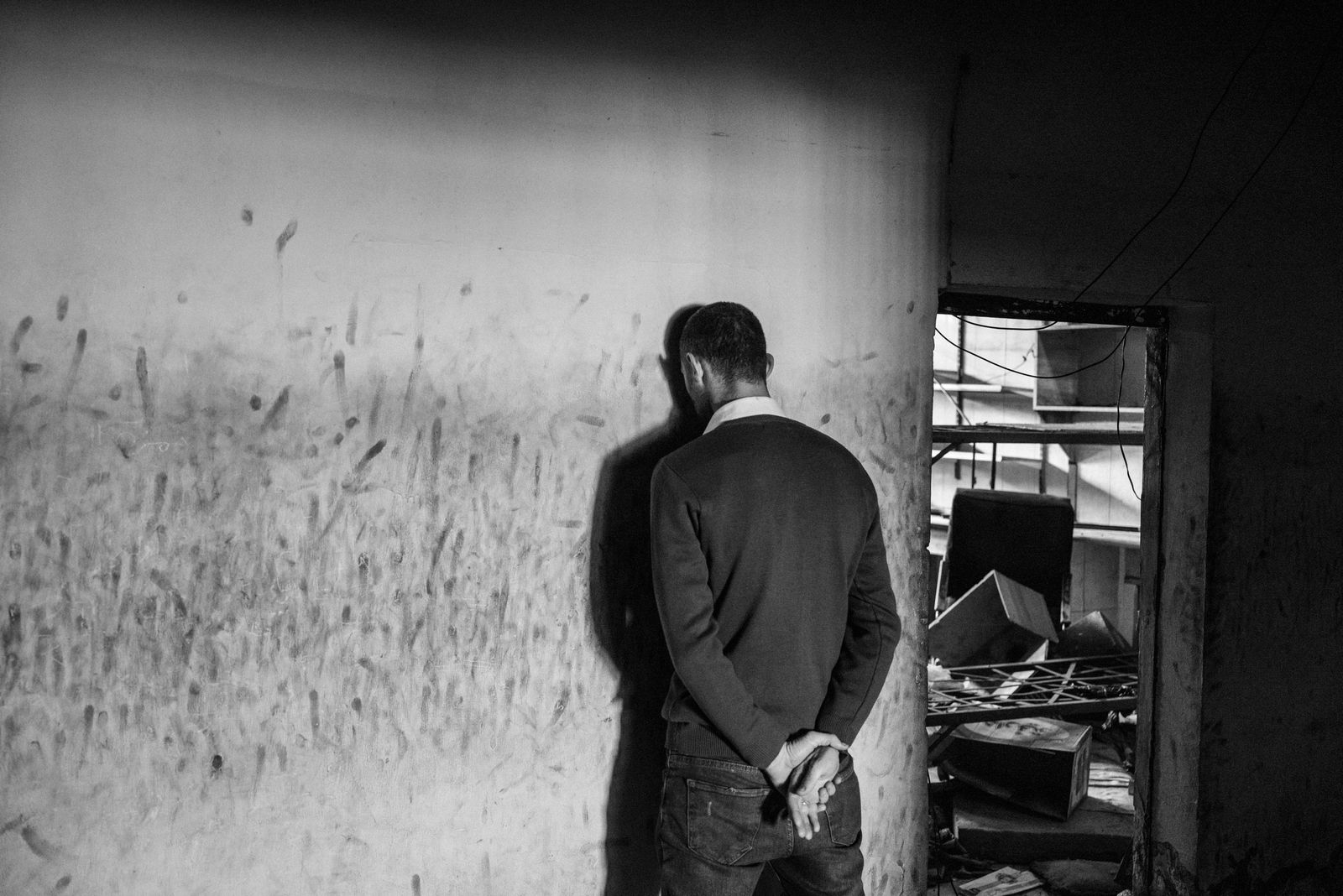 A blackandwhite photograph of a person with their head against the wall.