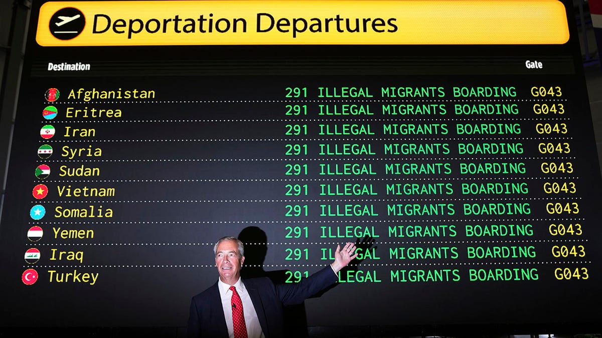British Reform party leader Nigel Farage stands in from a large sign about illegal immigration.
