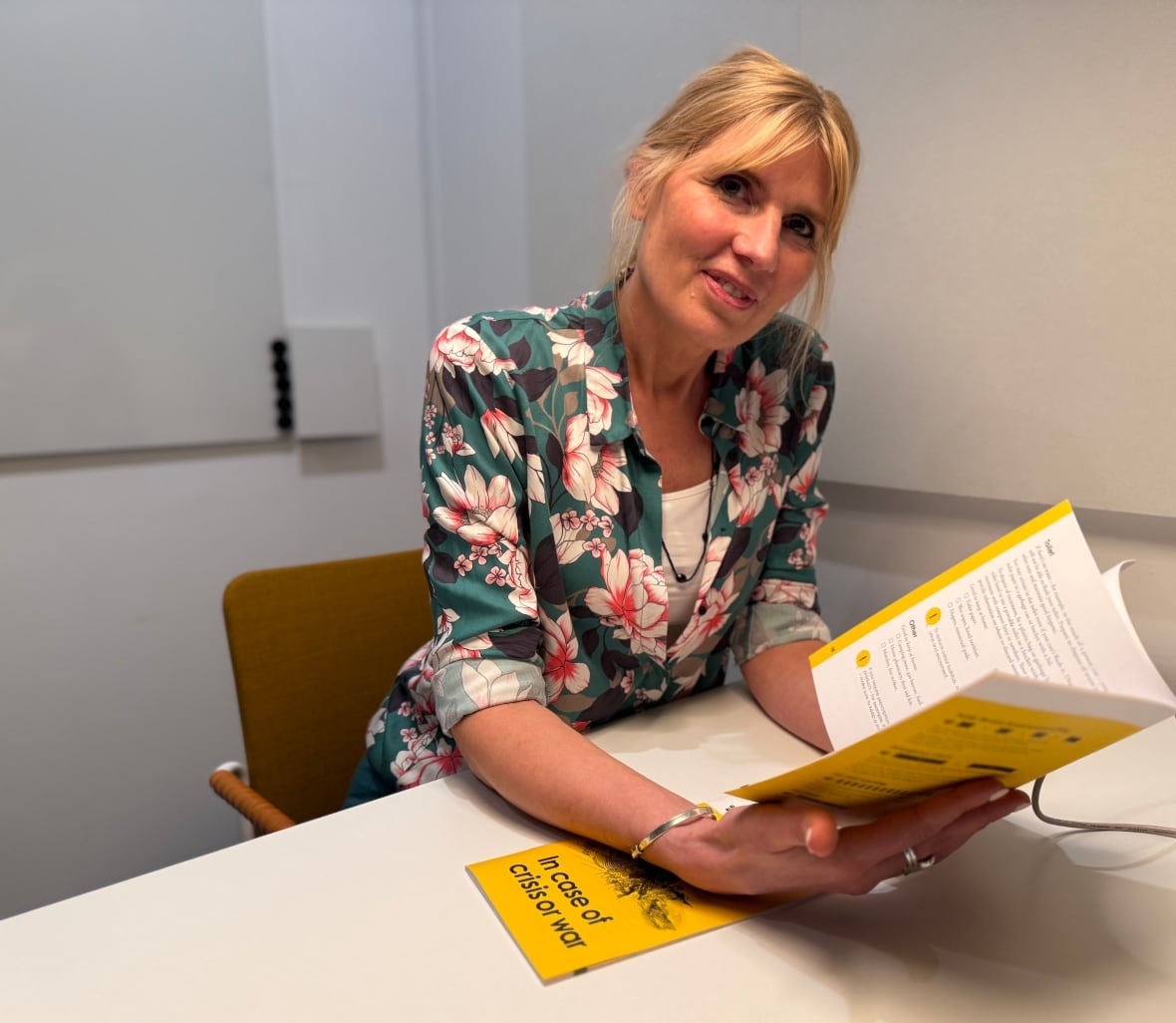 A woman with blonde hair wearing a green shirt reads a pamphlet