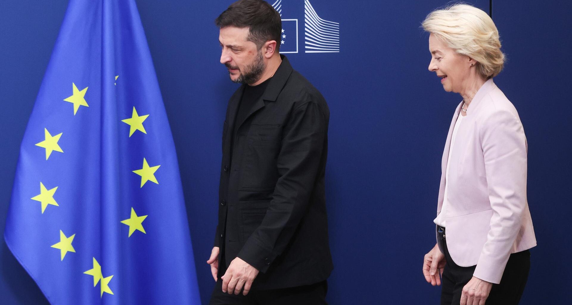Der ukrainische Präsident Selenskyj und EU-Kommissionspräsidentin von der Leyen stehen vor einem blauen Hintergrund mit einer europäischen Flagge.