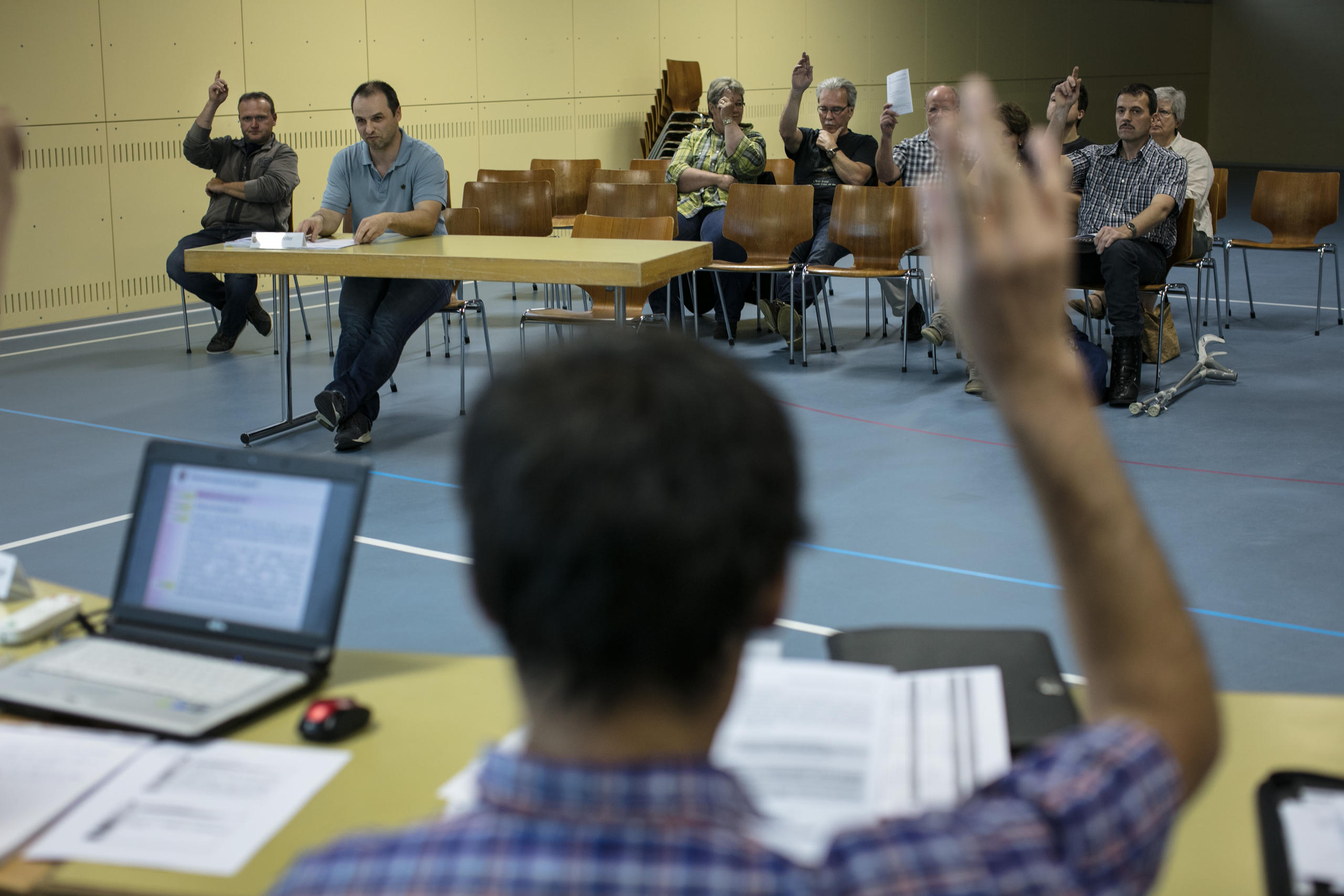 Eine Gruppe von Menschen sitzt in einer Halle, einige heben die Hände.