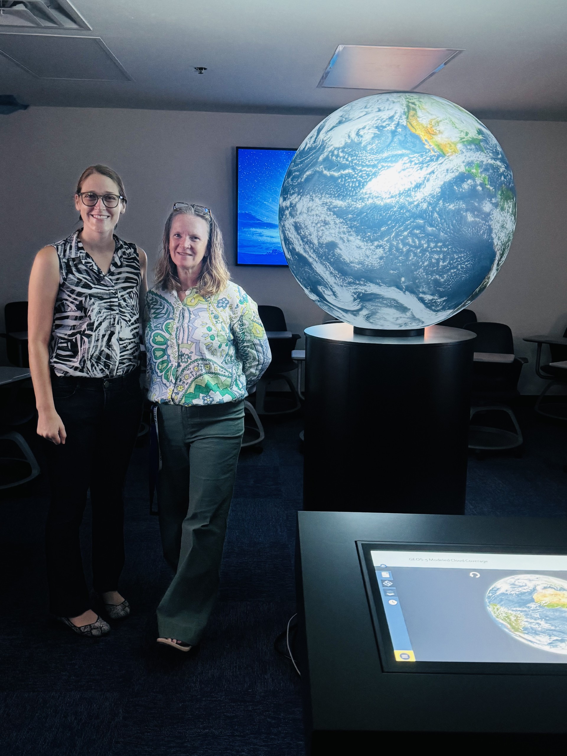 Jane Southworth and Gaby Hamerlinck standing in front of the OmniGlobe, a massive sphere with the Earth's surface projected onto it.