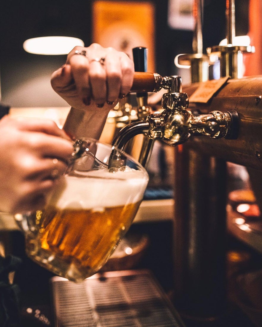 Bartender tapping a fresh, foamy beer into a glass mug at Tommi's Burger Joint in Selfoss, Iceland.