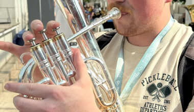 A young man plays a brass instrument in an atrium with a glass ceiling.