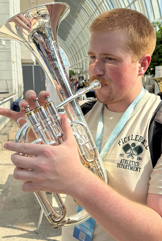 A young man plays a brass instrument in an atrium with a glass ceiling.