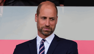 Prince William wearing a suit and tie in front of a pink and white background