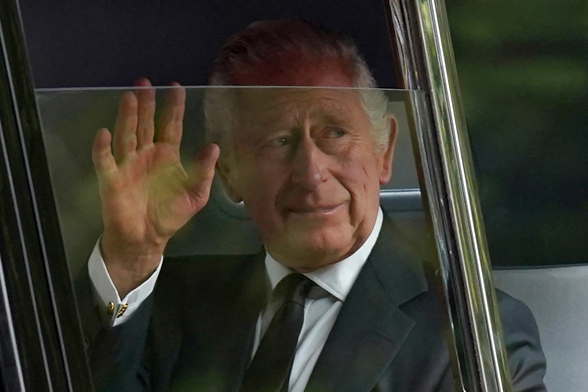 King Charles III waving from a car.