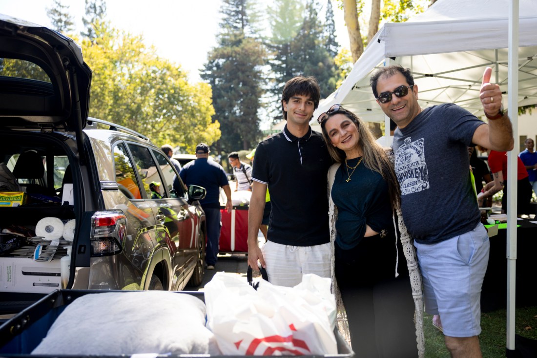 A family poses outdoors on a sunny day in front of a white tent.