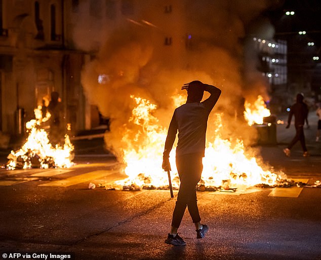 A young person walks past fires in a street, in Lausanne, on August 25, 2025, following Marvin's death