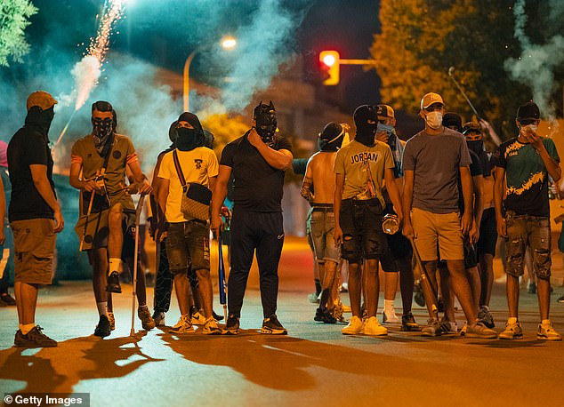 Protesters wearing masks and balaclavas hold chains, sticks and baseball bats during the fourth night of riots on July 14, 2025 in Torrepacheco, in the province of Murcia, Spain