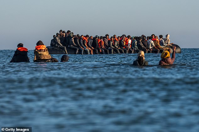 Migrants wade into the sea to board a dinghy to cross the English Channel on August 25, 2025
