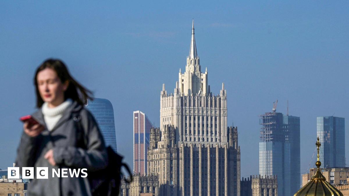 Photograph showing a woman looking at her phone as she walks across a bridge in central Moscow - with the Russian Foreign Ministry building in the background