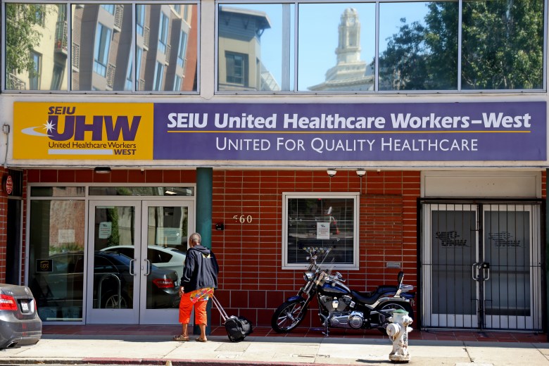 Storefront of SEIU United Healthcare Workers-West with a person pulling a suitcase and a motorcycle parked nearby.