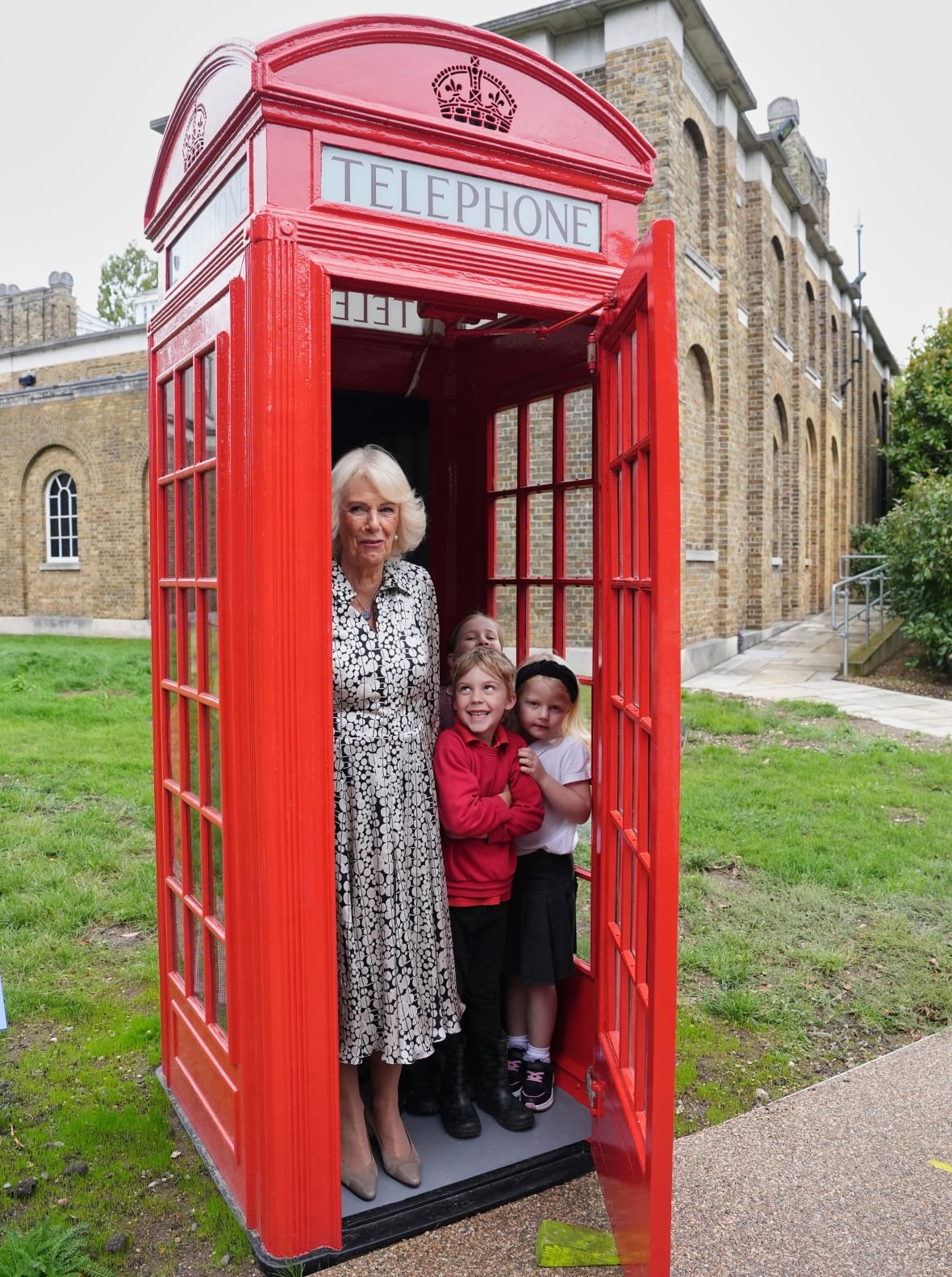 An adult and several children stand inside a red telephone box.