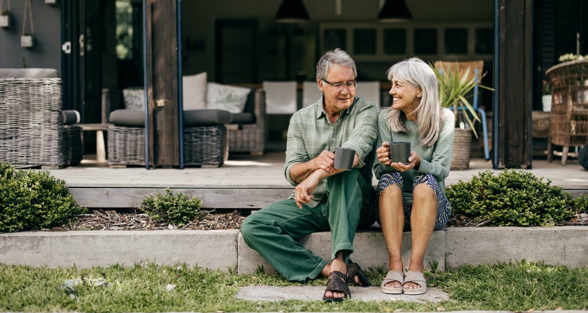 With coffee in hand, a senior couple in their 60s embraces a quiet moment, appreciating the beauty of their home.