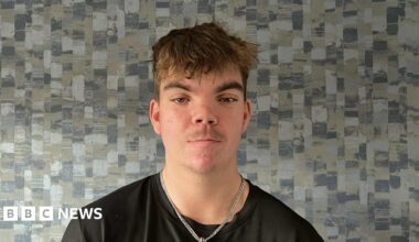 The picture features a woman with blonde hair and wearing a black jacket. Behind Siobhan is a white wall with three large rectangular windows