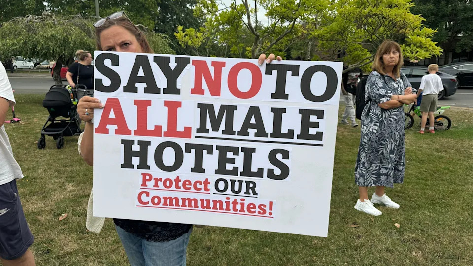 A female protestor holds up a sign saying 'say no to all male hotels. Protect our communities. 