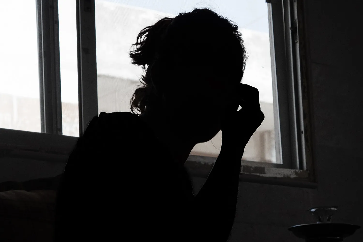 The silhouette of a woman in a window with her hand to her face.