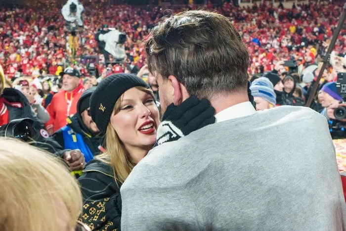 A woman in a beanie and jacket is facing a man with his back to the camera at a crowded sports event