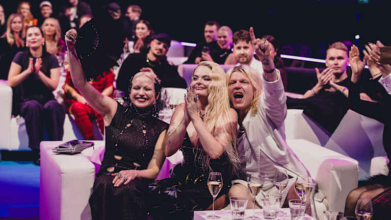 Last year's UMK winner, Erika Vikman surrounded by people sitting in easy chairs, cheering and applauding.