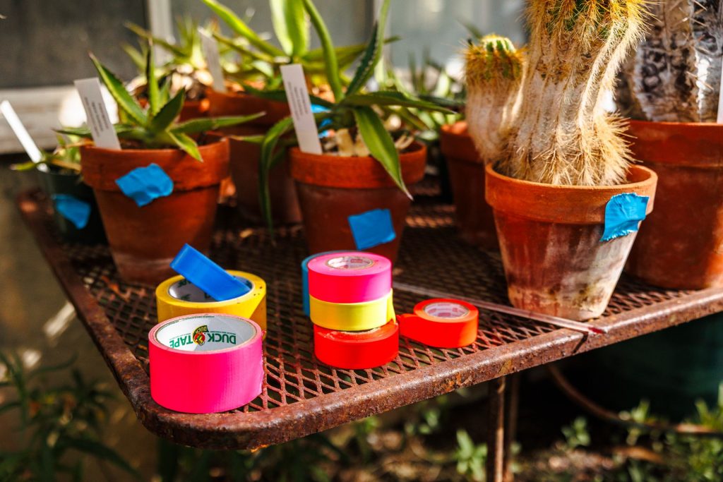 multi colored rolls of tape on a table next to potted plants
