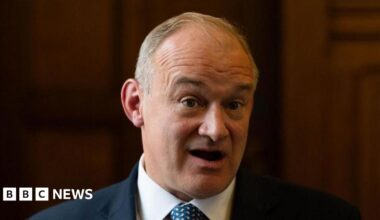 Ed Davey with mouth open, against a dark background