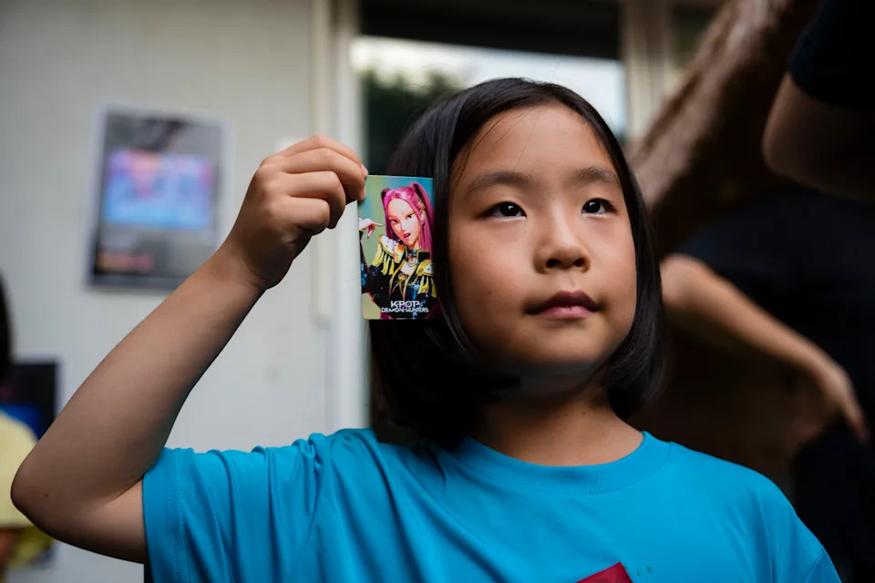 Lee Eun-ha, 7, holds a photo card of Mira, a member of the girl group Huntr/x from the movie, after the sing-along. Lee said she watched the movie at least 10 times. - (Jintak Han/The Washington Post)