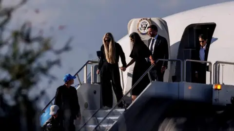 Getty Images Usha Vance is hand in hand with Erika Kirk, both dressed in black, as they disembark from Air Force Two plane in Arizona with JD Vance behind them