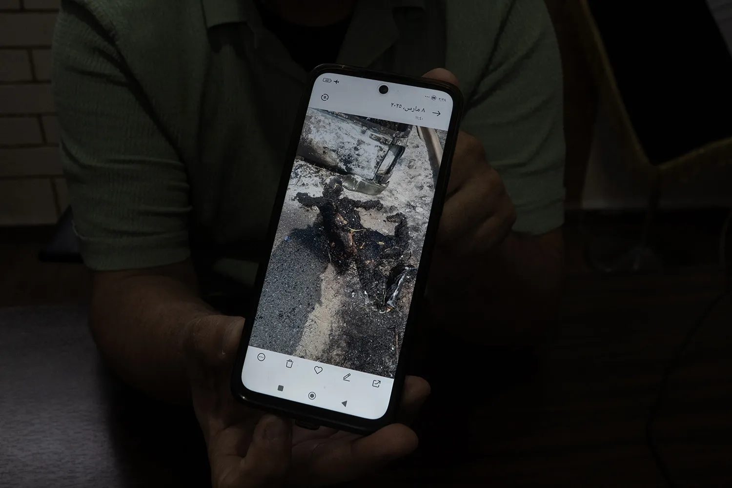 A man holds up a phone screen displaying an image of a burned body.