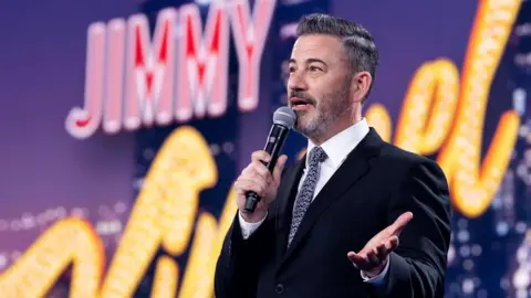 Getty Images Jimmy Kimmel speaking into a microphone in front of a giant sign bearing his name in May 2025