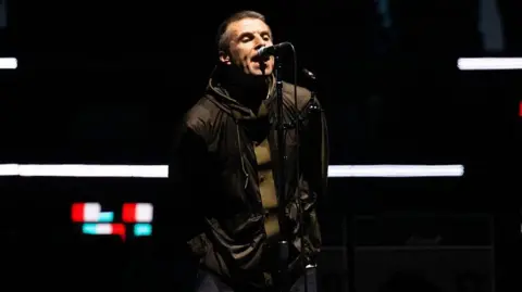 Getty Images Oasis singer Liam Gallagher sings into a microphone with his hands behind his back at the opening night of the band's reunion tour in Cardiff, Wales