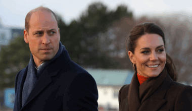 Kate Middleton wearing a brown coat and smiling next to Prince William