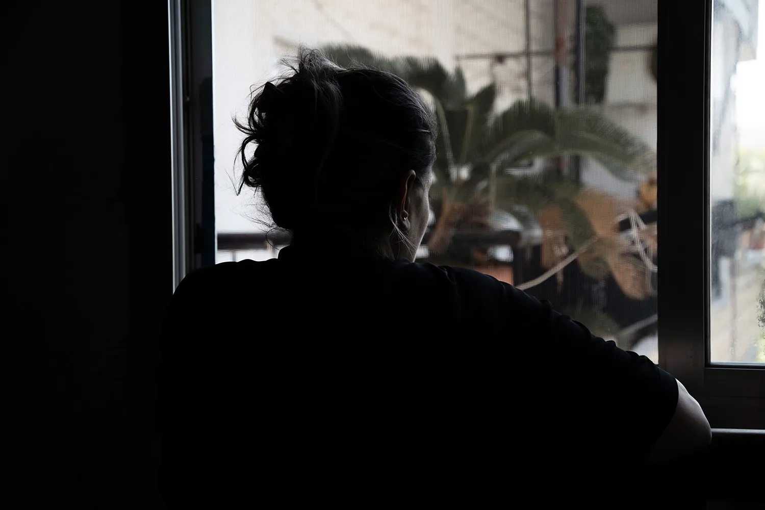The silhouette of a woman looking out of a window.