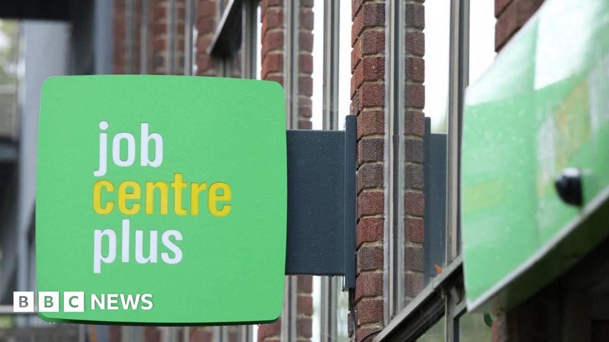 A close up of a green sign hanging off a building that reads "job centre plus". The word "centre" is in yellow and the other two words are in white.