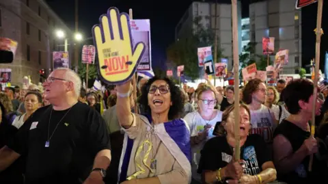 EPA/shutterstock A woman in the crowd holds up a poster of a yellow hand that says 'bring them home now'