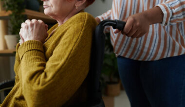 Close-up of senior woman with disability sitting in wheelchair with caregiver standing behind her