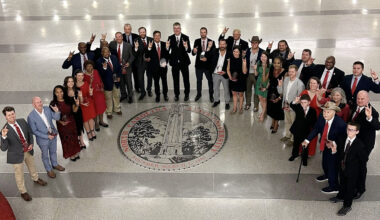 a group of people stand together in front of the NC State emblem on a marble floor