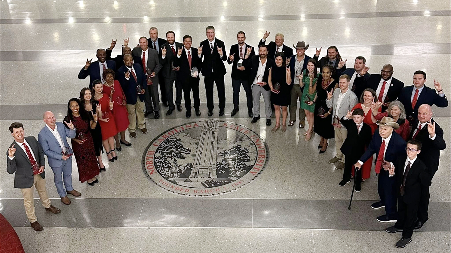 a group of people stand together in front of the NC State emblem on a marble floor