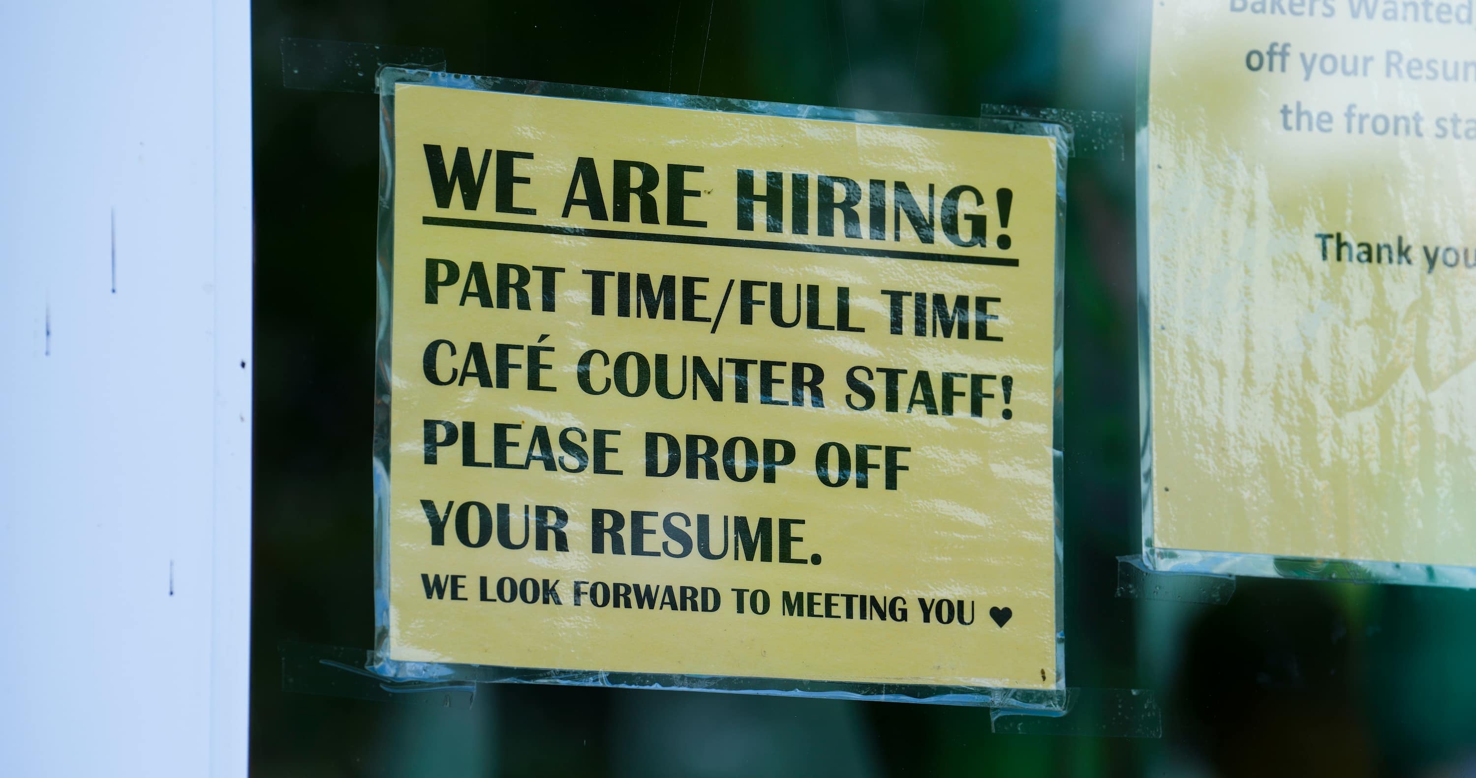 A sign on a business that says: We are hiring! Part time/full time cafe counter staff. Please drop off your resumé. We look forward to meeting you. 