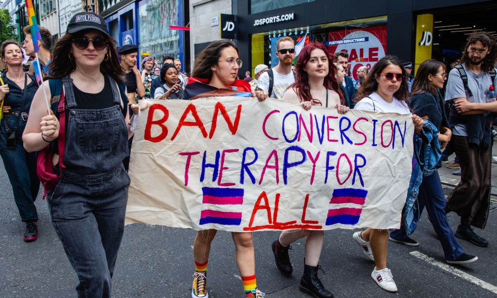 Activists hold a sign reading "ban conversion therapy for all."