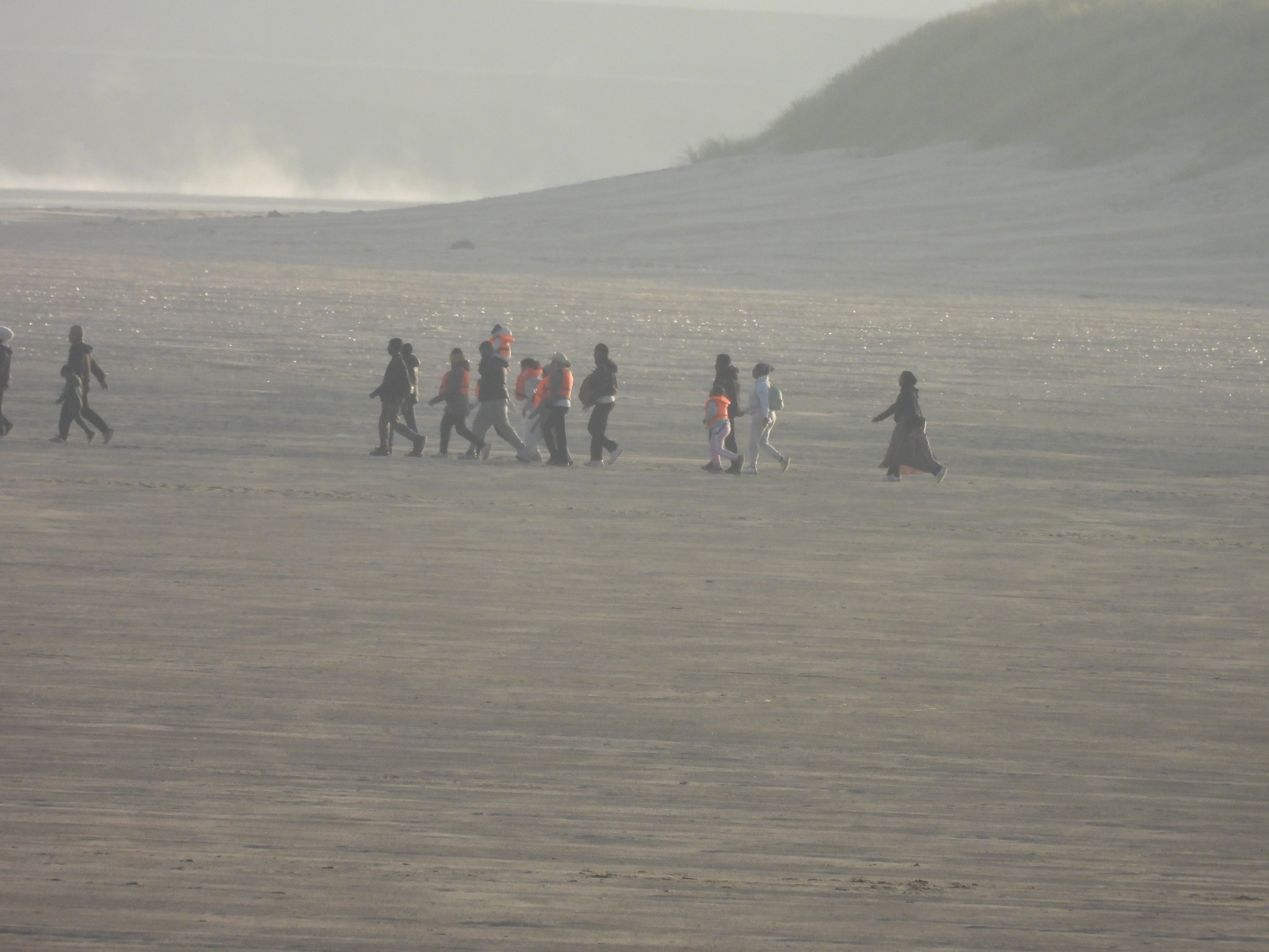 A group of migrants - including women and children - head across the beach to a boat waiting in the shallows