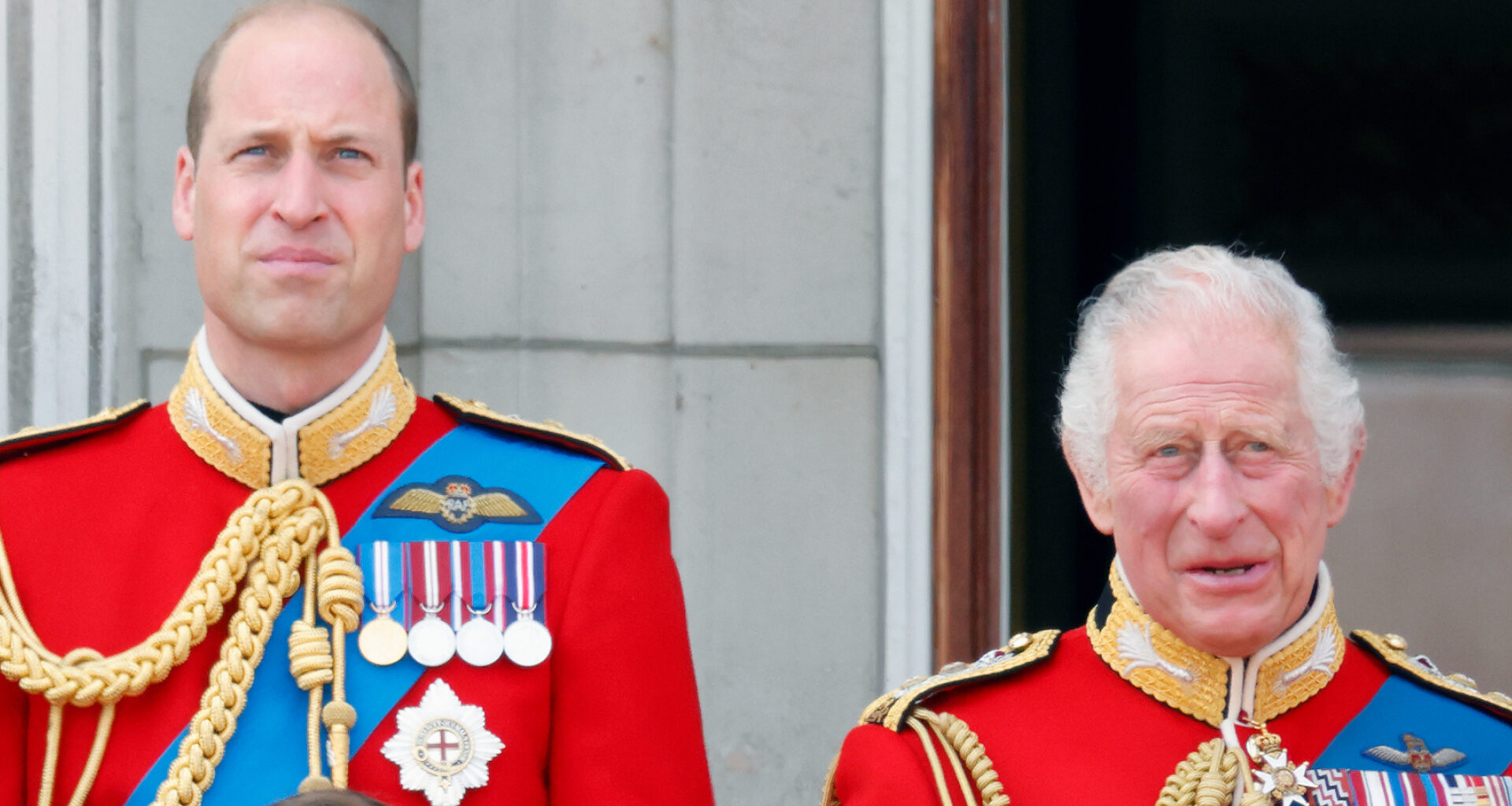 Prince William and King Charles wear red military uniforms as they stand on the Buckingham Palace balcony